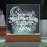 A wooden LED acrylic night light displaying the quote 'THE SKY HAS MILLIONS OF STARS BUT NONE SHINE AS BRIGHT AS YOU' in white script, set against a dark background with a warm glow.
