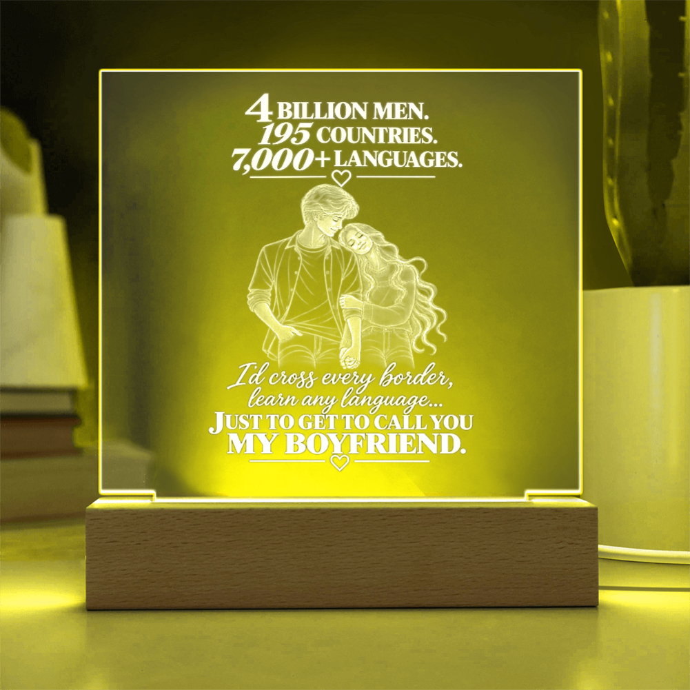 A rectangular acrylic LED night light with a wooden base, glowing with a warm yellow light. The front features a white laser-engraved illustration of a couple from behind with hearts and romantic text, set against a softly blurred home background.