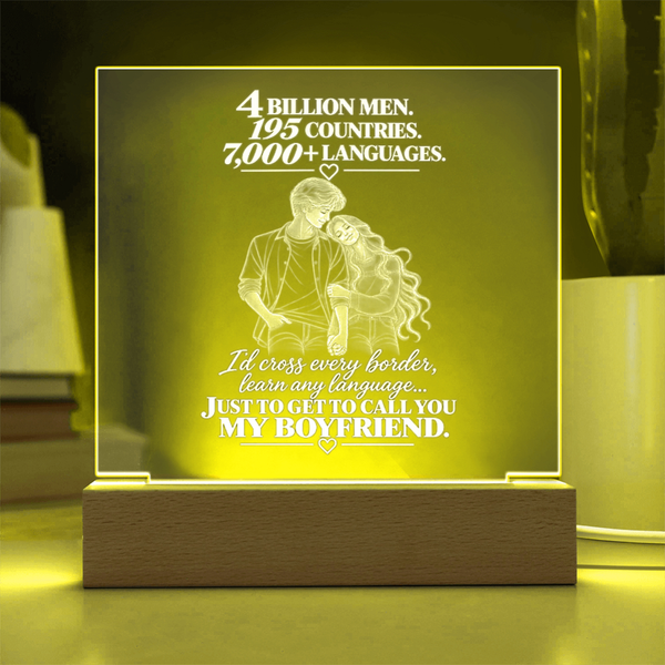 A rectangular acrylic LED night light with a wooden base, glowing with a warm yellow light. The front features a white laser-engraved illustration of a couple from behind with hearts and romantic text, set against a softly blurred home background.