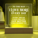 A rectangular acrylic LED night light with engraved white text on a wooden base, glowing with a warm yellow light in a home setting.