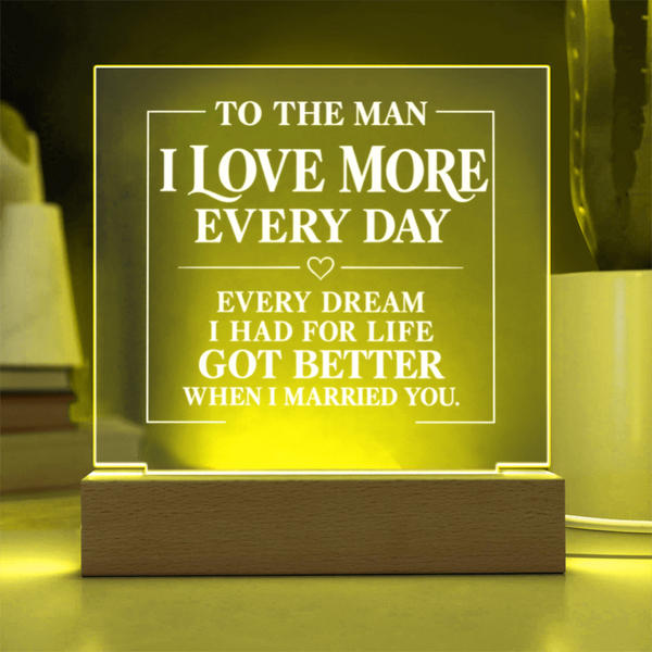 A rectangular acrylic LED night light with engraved white text on a wooden base, glowing with a warm yellow light in a home setting.