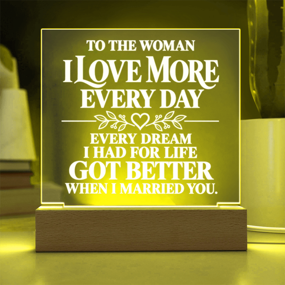 A rectangular acrylic LED night light with a wooden base, glowing with a warm yellow light. The clear panel features white printed text that reads, 'TO THE WOMAN I LOVE MORE EVERY DAY EVERY DREAM I HAD FOR LIFE GOT BETTER WHEN I MARRIED YOU.