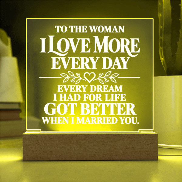 A rectangular acrylic LED night light with a wooden base, glowing with a warm yellow light. The clear panel features white printed text that reads, 'TO THE WOMAN I LOVE MORE EVERY DAY EVERY DREAM I HAD FOR LIFE GOT BETTER WHEN I MARRIED YOU.