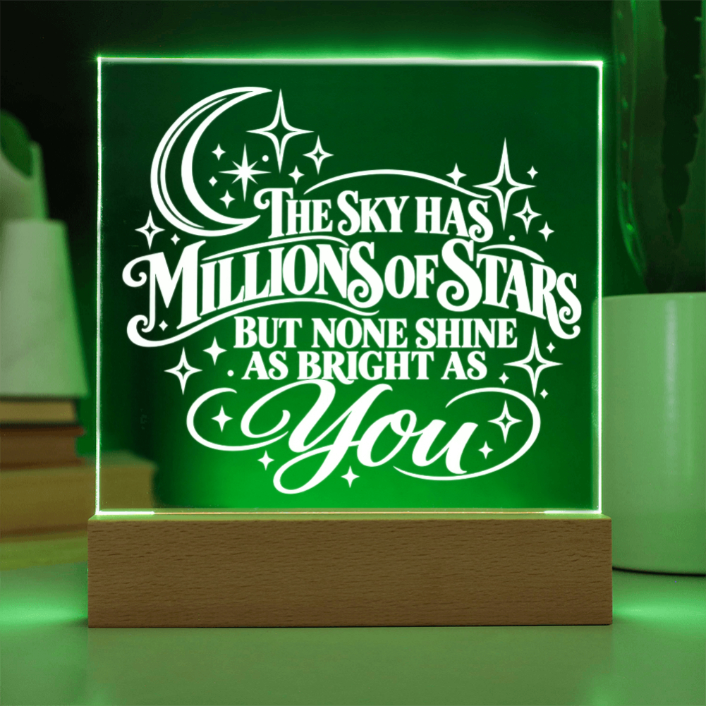 A glowing LED acrylic lamp with a wooden base, displaying the quote 'THE SKY HAS MILLIONS OF STARS BUT NONE SHINE AS BRIGHT AS YOU' in white against a green illuminated background.