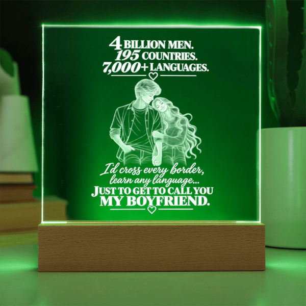 A glowing acrylic LED cube lamp with a wooden base, featuring white engraved text and an illustration of a couple, set against a dark background with green light illumination.