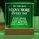 A rectangular acrylic LED light sign on a wooden base, glowing green with white text that reads, 'TO THE MAN I LOVE MORE EVERY DAY EVERY DREAM I HAD FOR LIFE GOT BETTER WHEN I MARRIED YOU.'.