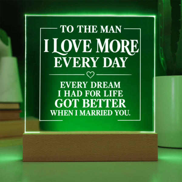 A rectangular acrylic LED light sign on a wooden base, glowing green with white text that reads, 'TO THE MAN I LOVE MORE EVERY DAY EVERY DREAM I HAD FOR LIFE GOT BETTER WHEN I MARRIED YOU.'.