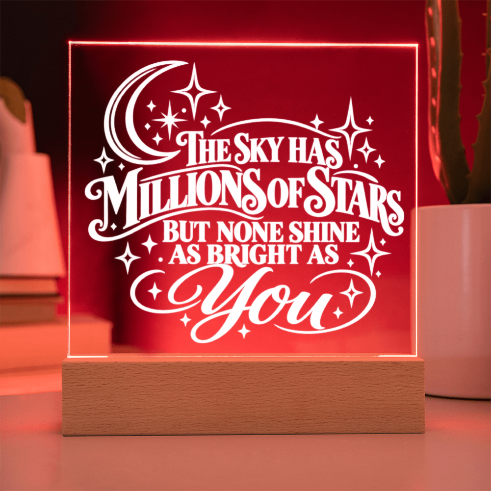 A square acrylic LED night light on a wooden base, glowing with a warm red light and featuring the white text 'THE SKY HAS MILLIONS OF STARS BUT NONE SHINE AS BRIGHT AS You' with a crescent moon and stars.