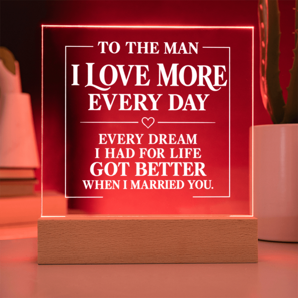 A rectangular acrylic LED light sign on a wooden base, glowing red with white text that reads, 'TO THE MAN I LOVE MORE EVERY DAY EVERY DREAM I HAD FOR LIFE GOT BETTER WHEN I MARRIED YOU.'.