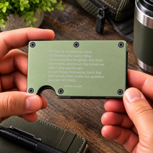 A person holds a slim olive green card holder wallet with a printed sentimental message for their dad. The wallet has rounded corners, four black screw holes, and a small curved cutout at the bottom.