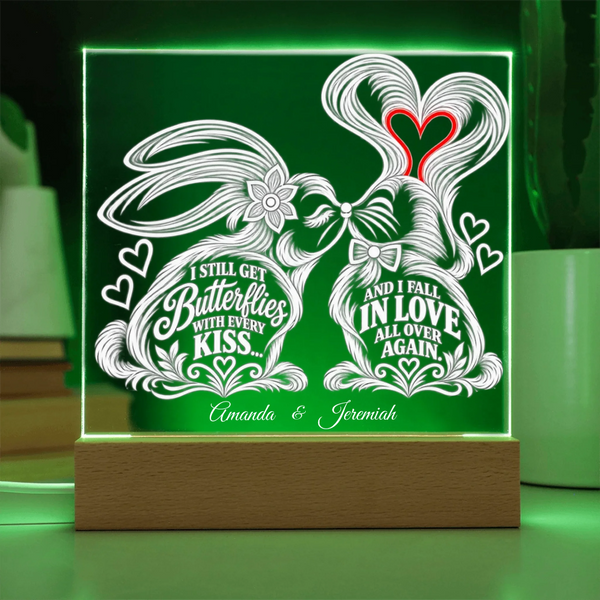A personalized acrylic LED night light on a wooden base, featuring two white line-art rabbits holding hearts with romantic quotes and the names 'Amanda & Jeremiah' at the bottom, glowing green in the background.
