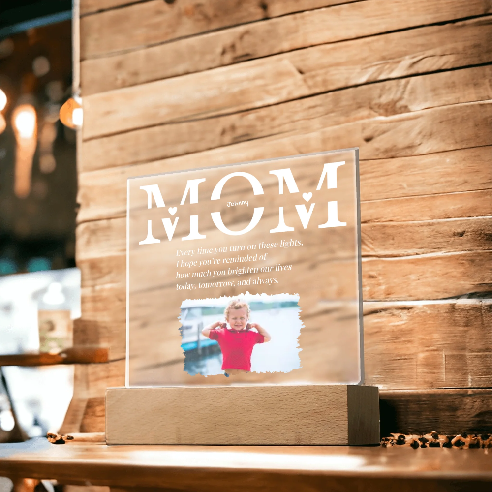 Clear acrylic plaque with 'MOM' and a photo of a child on a wooden stand against a wooden wall.