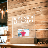 Clear acrylic plaque with 'MOM' and a photo of a child on a wooden stand against a wooden wall.