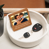 A personalized leather keychain wallet card with a photo of a father and son and a sentimental message, displayed in a white woven basket next to a car key fob and keys.
