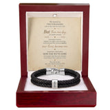 A black braided leather bracelet with a silver-toned clasp, presented inside an open reddish-brown wooden gift box. The box contains a cream-colored card with a romantic poem titled 'How Far We've Come'.