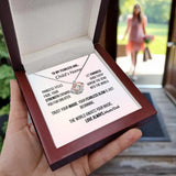 Necklace with a message card held by a hand, with a blurred background of a woman walking outdoors.