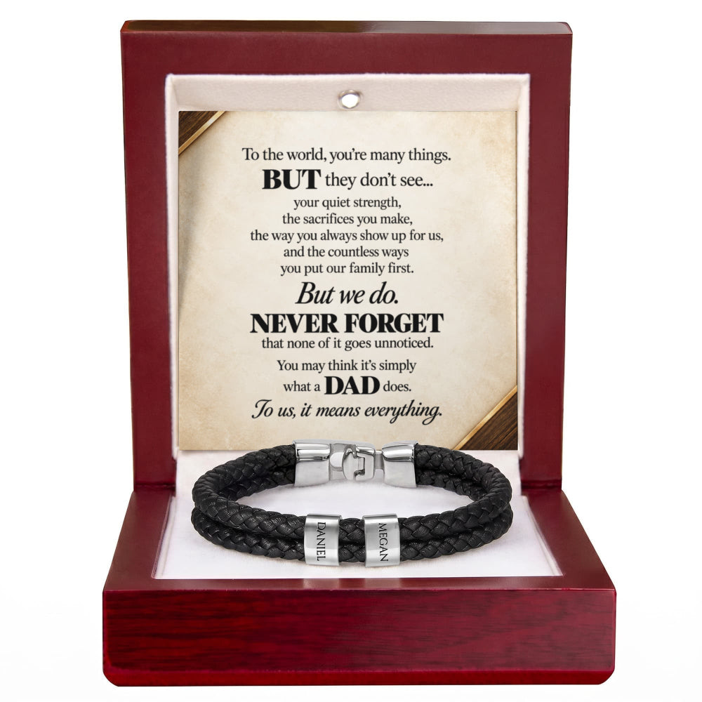 A black braided cord bracelet with silver-toned metal clasps, presented inside an open reddish-brown wooden gift box. The box contains a printed memorial-style message card addressed to a father, with the bracelet displayed below on a white insert.