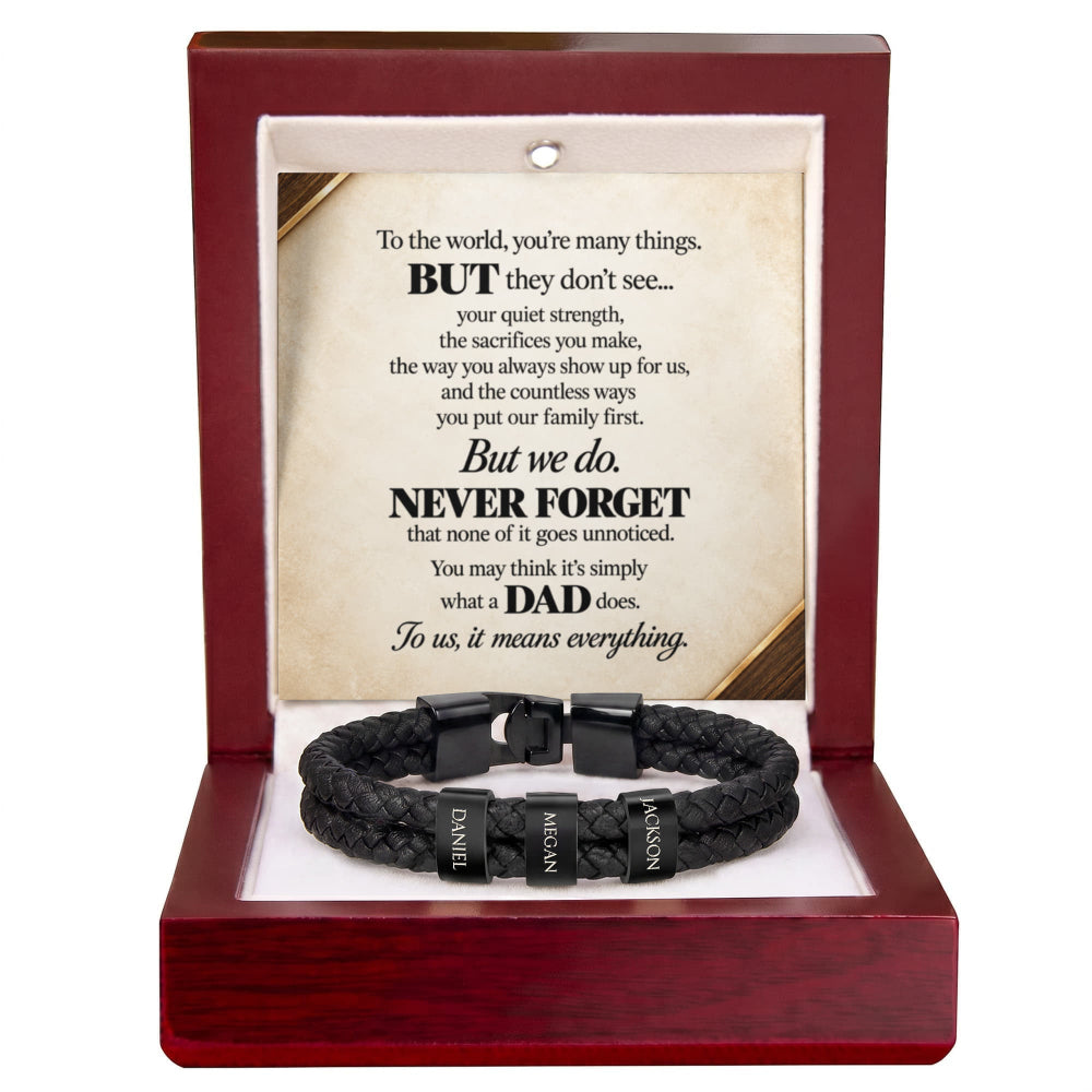 A black braided cord bracelet with three black metal name tags engraved with 'DAD', 'MATHER', and 'FATHER', presented inside an open dark red wooden gift box with a sentimental poem printed on the insert card.