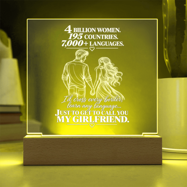 A rectangular acrylic LED night light with a wooden base, glowing with a warm yellow light. The front features a white laser-engraved illustration of a couple from behind with hearts and romantic text, set against a softly blurred home background.
