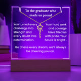 Decorative plaque with  text and a graduation cap symbol, illuminated with purple light.