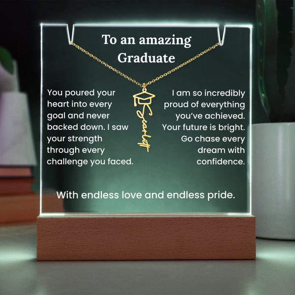 Decorative plaque with a gold necklace and graduation cap pendant, featuring an engraved name, on a dark background.