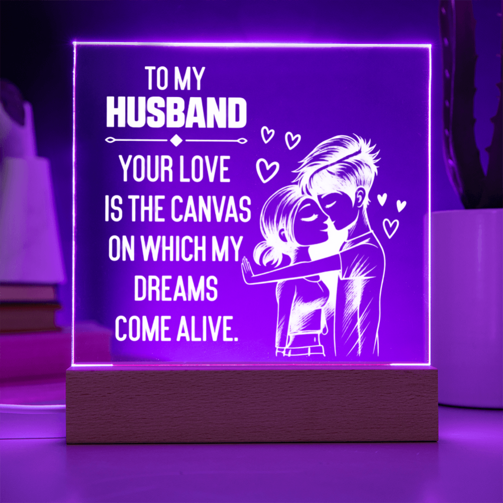 A rectangular acrylic LED night light on a wooden base, glowing with purple light and featuring white text that reads, 'TO MY HUSBAND YOUR LOVE IS THE CANVAS ON WHICH MY DREAMS COME ALIVE,' plus a couple illustration and small hearts.