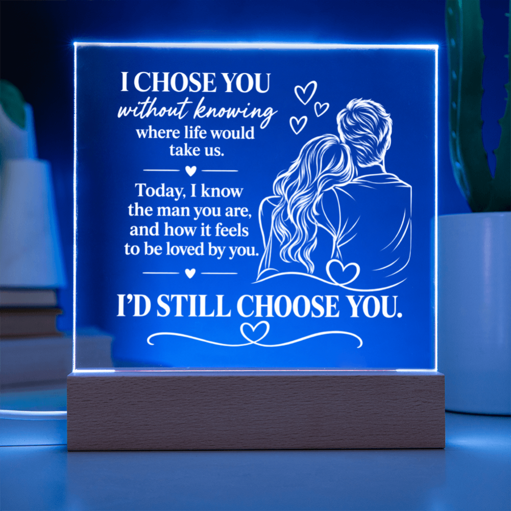 A rectangular acrylic LED night light on a wooden base, glowing with a blue light and featuring a romantic quote and an illustration of a couple, set against a softly blurred background.
