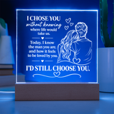 A rectangular acrylic LED night light on a wooden base, glowing with a blue light and featuring a romantic quote and an illustration of a couple, set against a softly blurred background.