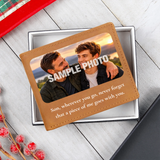 A custom photo wallet card with a tan faux-leather border, displayed inside a silver gift box on a light gray wood background. The card features a customizable sample photo of a young man and a sentimental message for 'Son'.