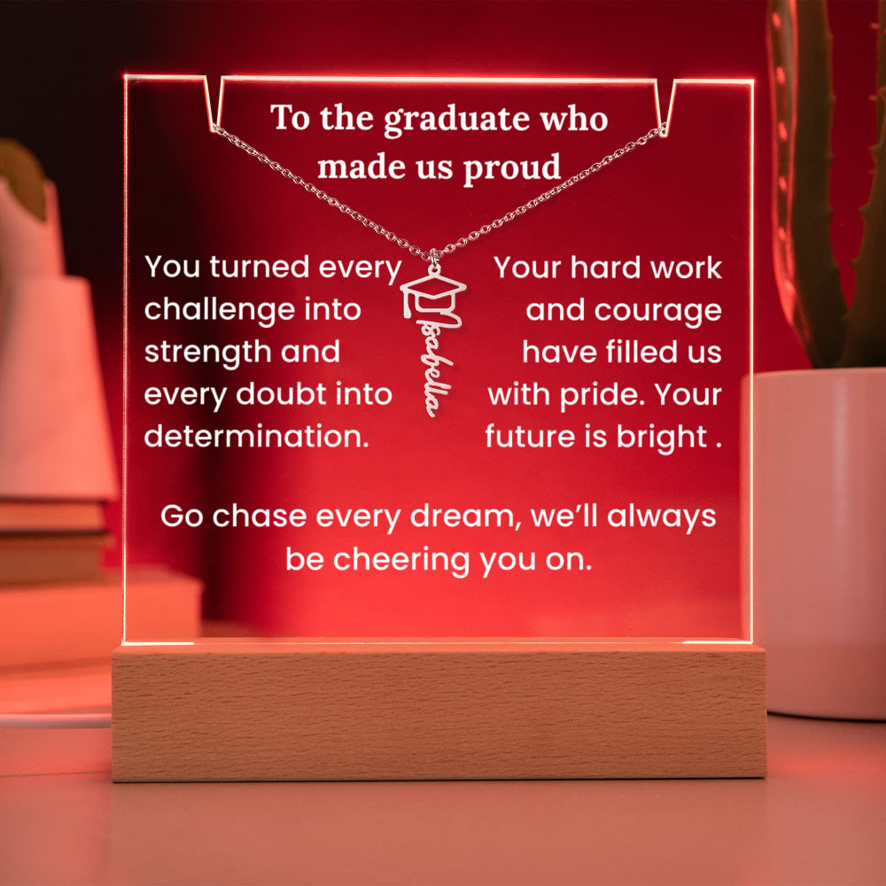Decorative plaque with graduation-themed message and necklace on a wooden base against a red background.