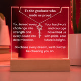Decorative plaque with graduation-themed message and necklace on a wooden base against a red background.
