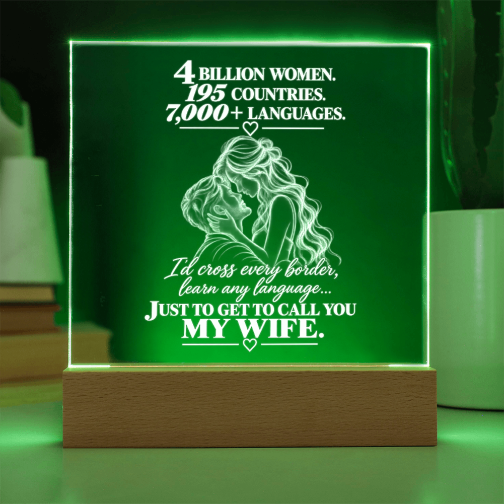 A rectangular acrylic LED lamp on a wooden base, glowing with green light and featuring white engraved text and an illustration of a couple, set against a softly blurred home background.