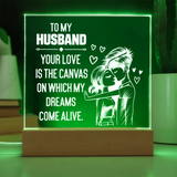A rectangular LED acrylic night light on a wooden base, glowing green with white text that reads, 'TO MY HUSBAND YOUR LOVE IS THE CANVAS ON WHICH MY DREAMS COME ALIVE,' plus a couple illustration and small hearts.