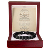 A black braided bracelet with engraved silver lettering on each bead, presented inside an open reddish-brown wooden gift box with a white insert and a sentimental quote card.