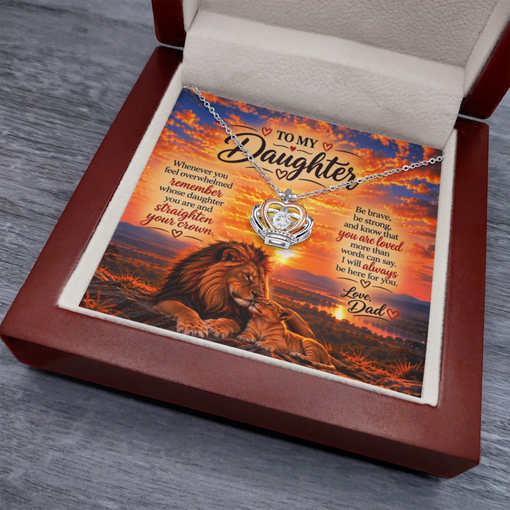 A silver necklace with a heart-shaped pendant is displayed inside an open reddish-brown gift box. The necklace rests on a printed card featuring a lion and sunset scene with the message 'To My Daughter'.