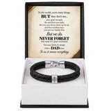 A black braided leather bracelet with silver-toned hardware displayed inside an open gift box. The box has a white interior and a black outer frame, with a printed message card inside the lid that reads 'But we.