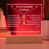 Graduation-themed necklace with engraved message on a wooden stand with red background
