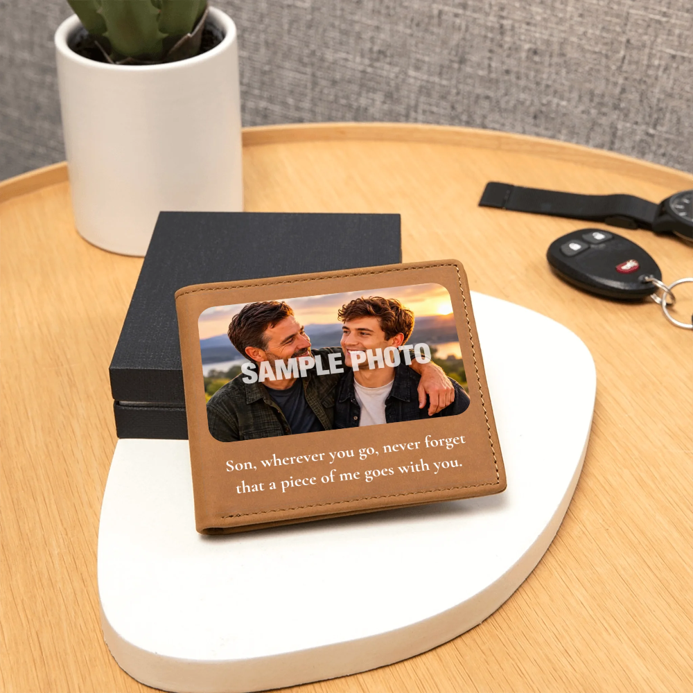 A personalized leather bifold wallet with a printed photo of two men and a sentimental quote, displayed on a white oval stand on a wooden table next to keys and a potted plant.
