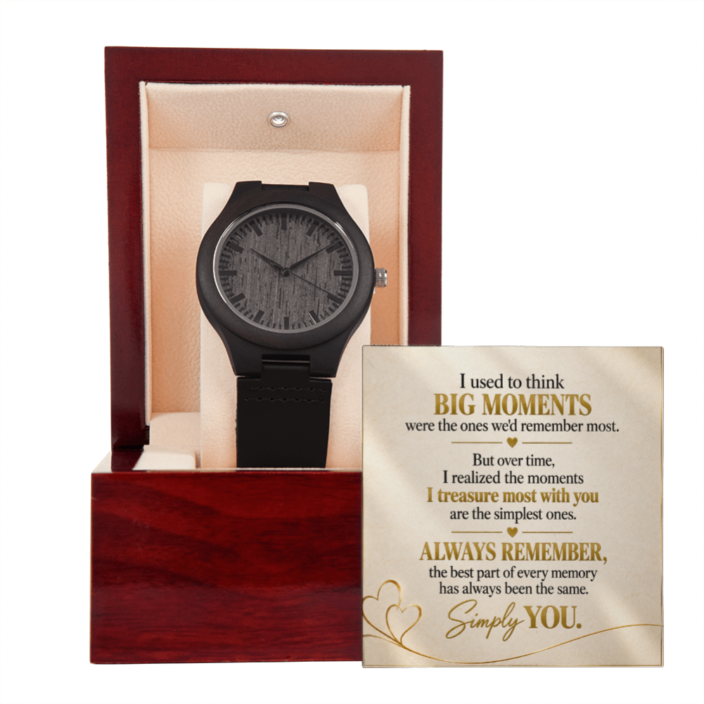 A black wooden wristwatch displayed inside an open reddish-brown presentation box with a cream interior, alongside a printed sentimental message card on a white background.