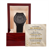 A black wooden wristwatch displayed inside an open reddish-brown presentation box with a cream interior, alongside a printed sentimental message card on a white background.
