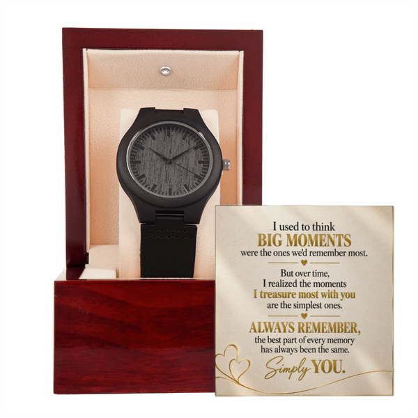 A black wooden wristwatch displayed inside an open reddish-brown presentation box with a cream interior, alongside a printed sentimental message card on a white background.