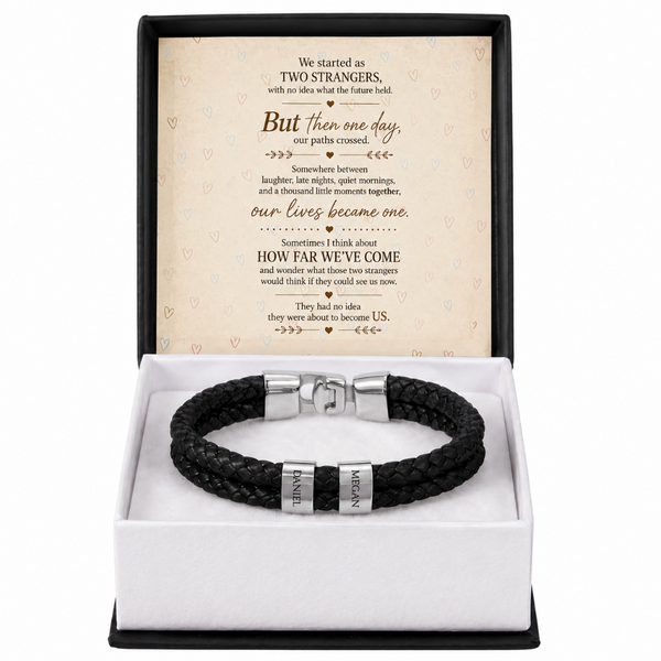 A black braided leather bracelet with silver-toned metal accents, presented in a white gift box with a black outer frame. The inside lid features a printed sentimental message card.