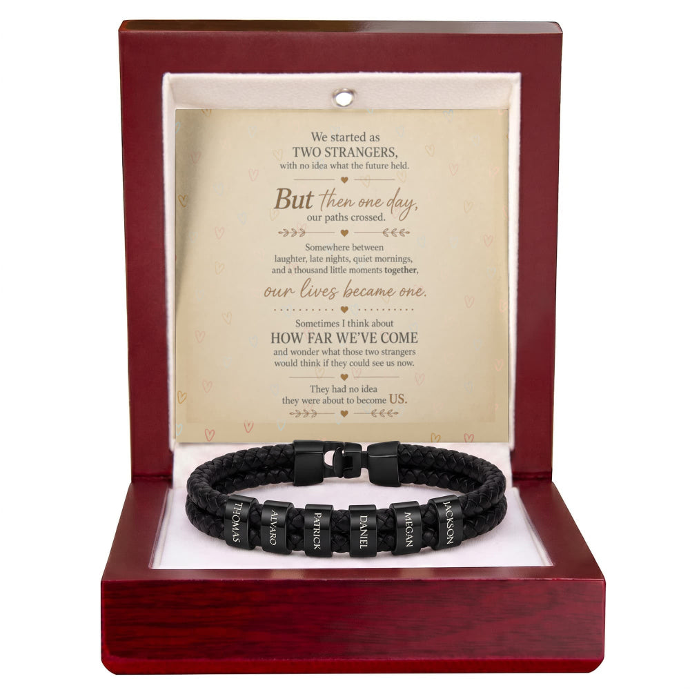 A black braided bracelet with engraved silver lettering on each bead, presented inside an open reddish-brown wooden gift box with a white insert and a sentimental quote card.