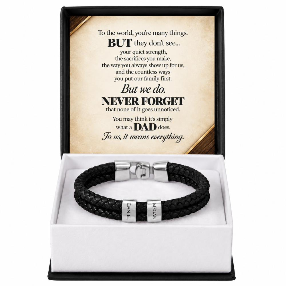 A black braided leather bracelet with silver-toned metal accents and engraved names, presented in an open white gift box with a black outer frame. The lid displays a sentimental message for a father.