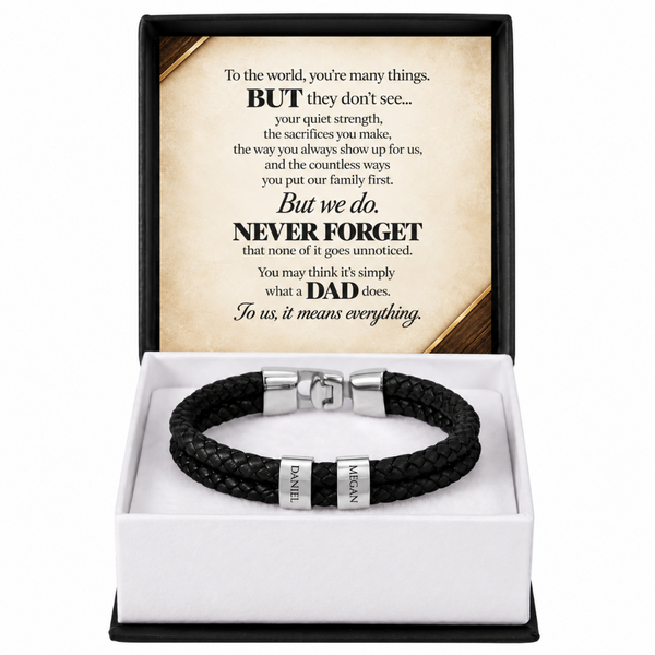 A black braided leather bracelet with silver-toned metal accents and engraved names, presented in an open white gift box with a black outer frame. The lid displays a sentimental message for a father.