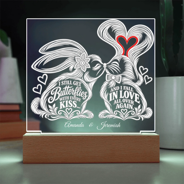 A personalized acrylic LED light sign on a wooden base, featuring two kissing rabbits with hearts and the words 'I Still Get Butterflies With Every Kiss.