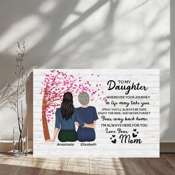 A personalized wooden sign with a printed illustration of two women sitting under a pink-blossomed tree, next to a block of sentimental text addressed to a daughter. The sign is displayed on a wooden floor against a wall with soft window shadows.