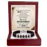 A black braided cord bracelet with silver engraved letter beads, presented inside an open dark red wooden gift box with a printed memorial message card.