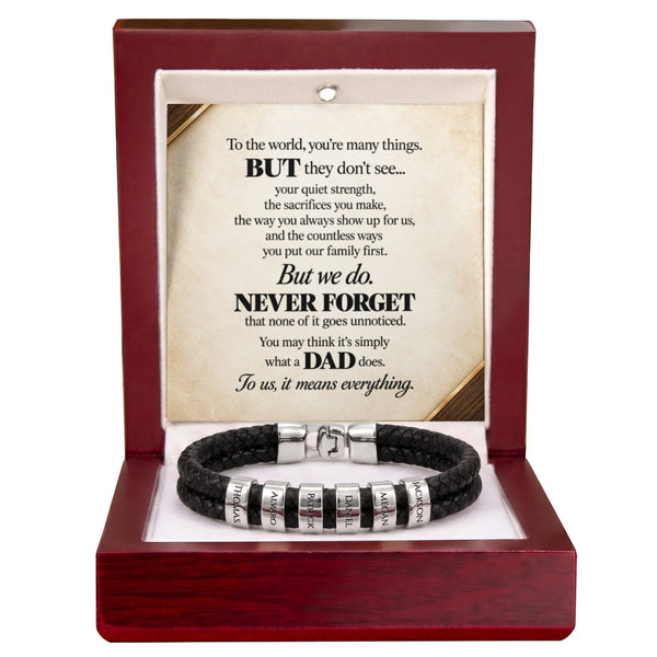 A black braided cord bracelet with silver engraved letter beads, presented inside an open dark red wooden gift box with a printed memorial message card.