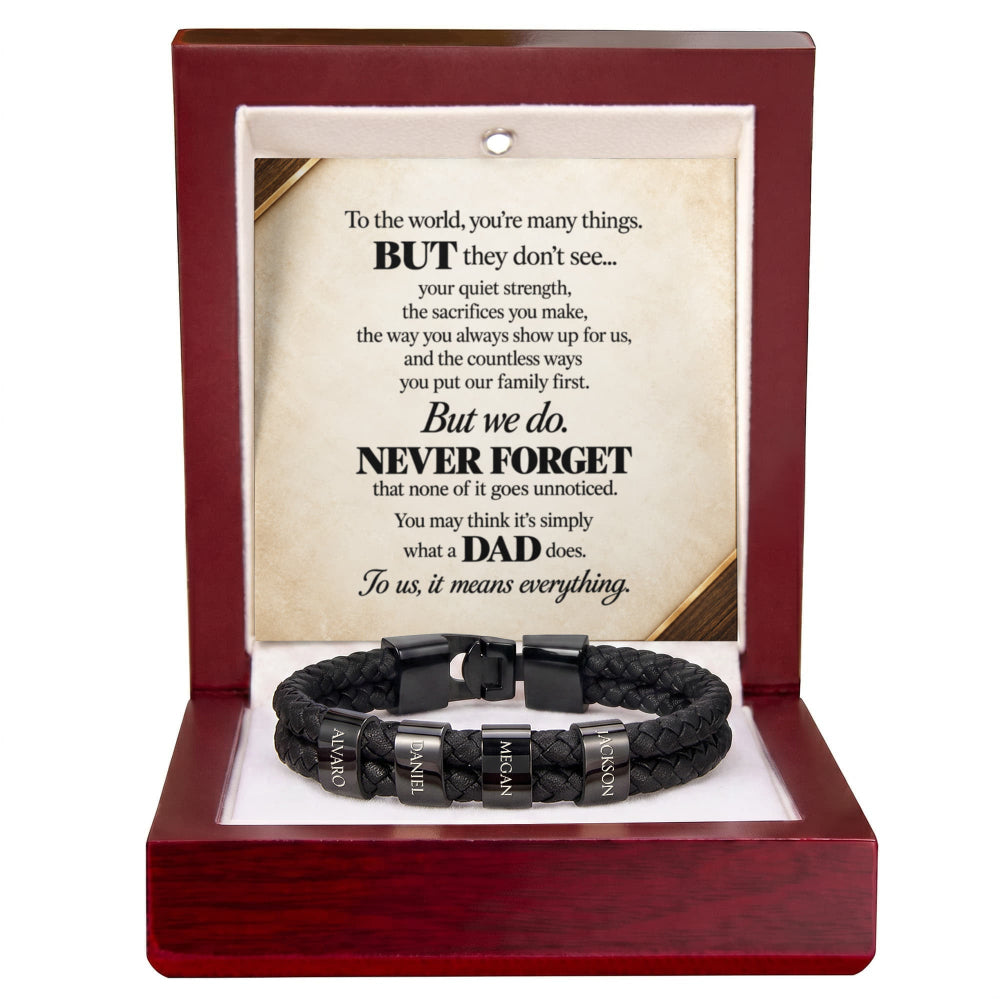 A black braided cord bracelet with silver engraved metal beads and a black clasp, presented inside an open reddish-brown wooden gift box. The box contains a printed message card dedicated to a father.